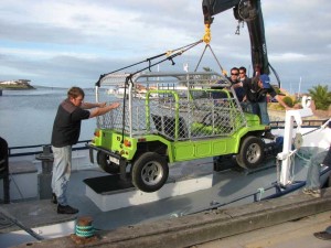 A picture of a green export Moke being loaded onto a small trawler.